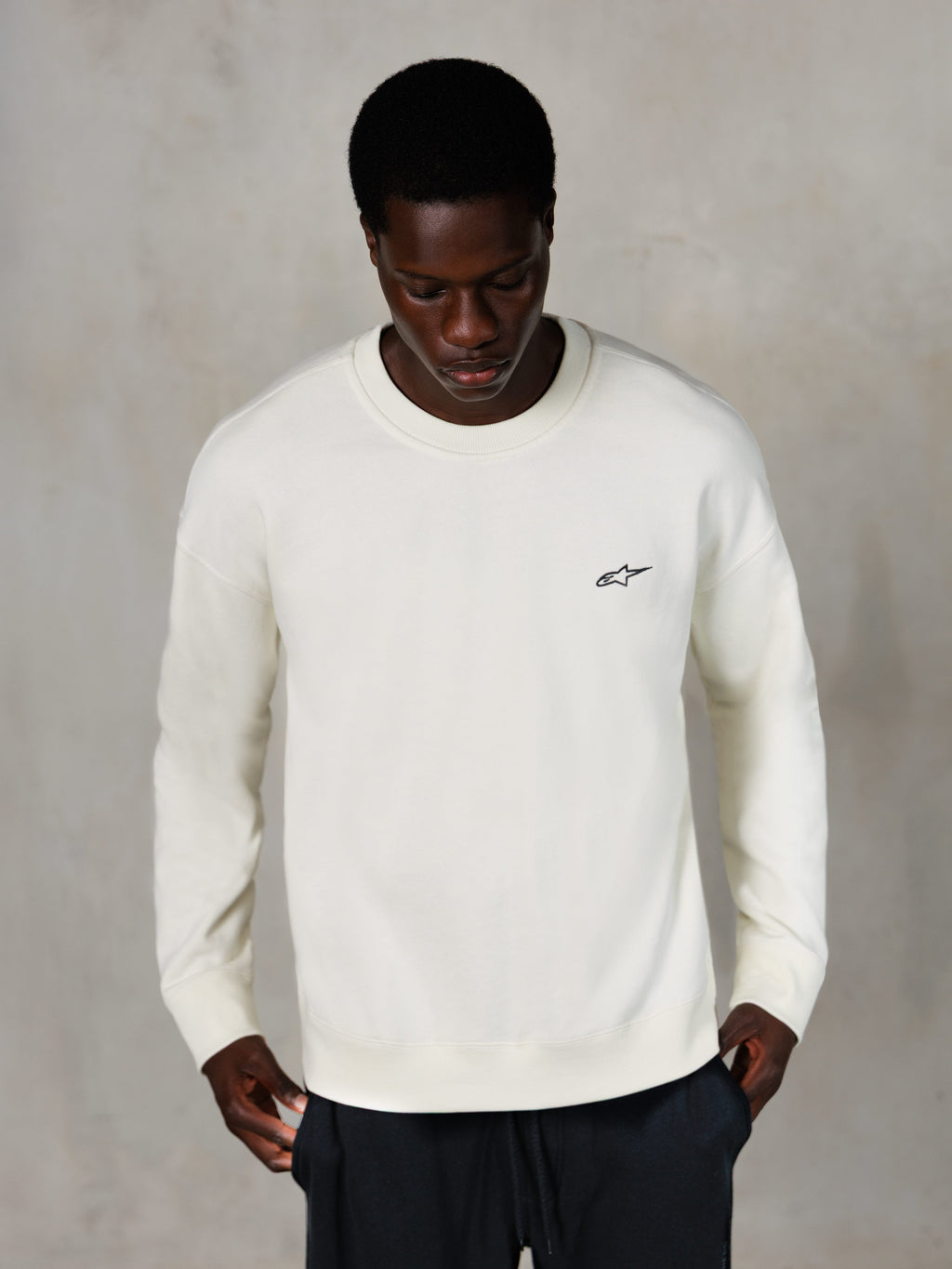 Alpinestars Essentials Ageless Crew, Rundhals-Sweatshirt, Off-White, kleines schwarzes Alpinestars-Logo auf der Brust, von einem Model getragen, lässige Lifestyle-Streetwear, hochwertiges weiches Fleece