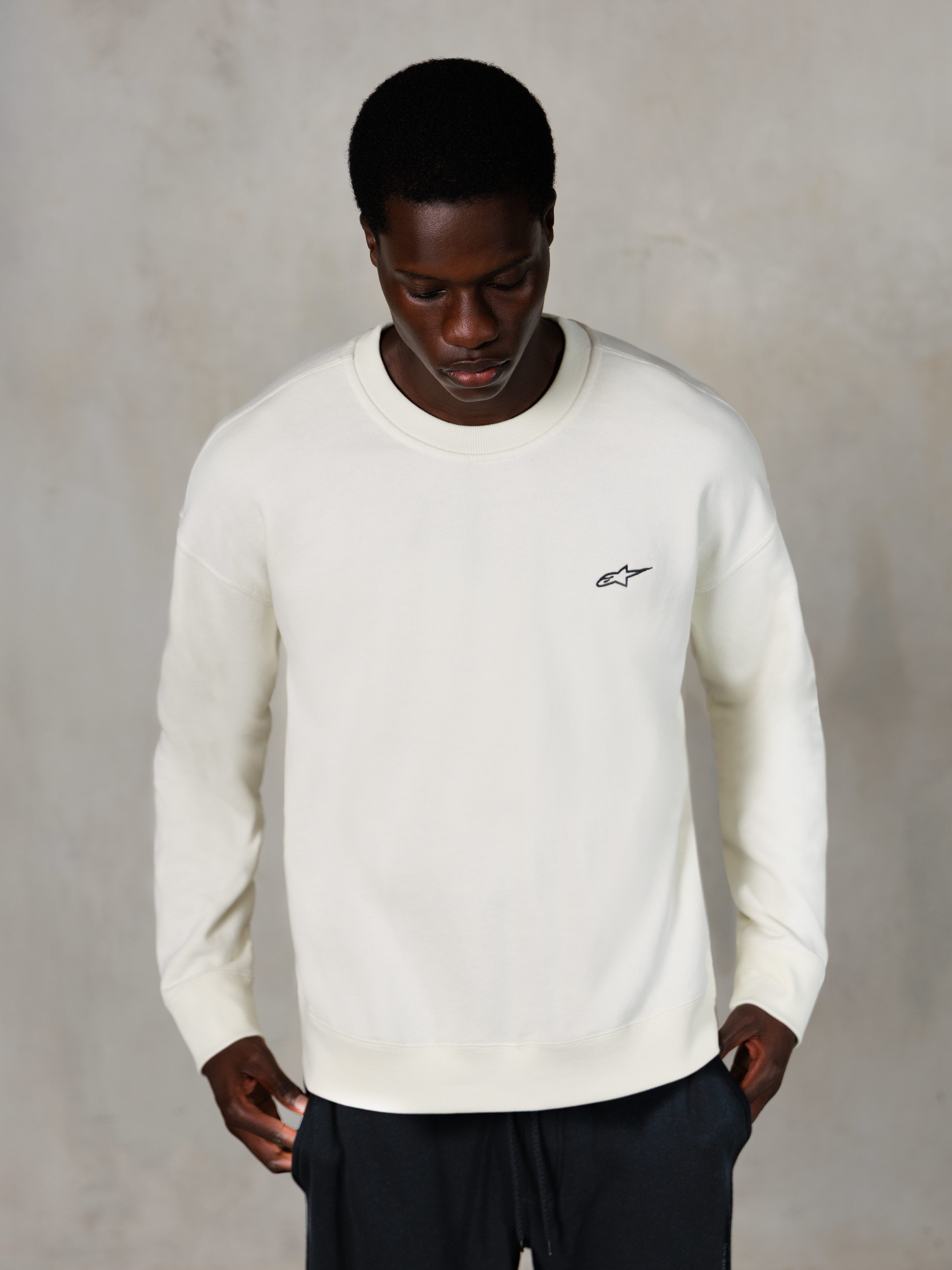 Alpinestars Essentials Ageless Crew, Rundhals-Sweatshirt, Off-White, kleines schwarzes Alpinestars-Logo auf der Brust, von einem Model getragen, lässige Lifestyle-Streetwear, hochwertiges weiches Fleece