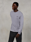 Alpinestars Essentials Ageless LS Tee, Langarm-T-Shirt, Silber, kleines schwarzes Logo auf der Brust, getragen von einem lächelnden Model mit dunkler Hose, entspannte zeitgemäße Passform, lässige Motorsport-Lifestyle-Bekleidung