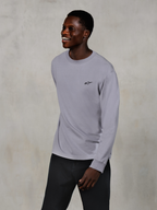 Alpinestars Essentials Ageless LS Tee, Langarm-T-Shirt, Silber, kleines schwarzes Logo auf der Brust, getragen von einem lächelnden Model mit dunkler Hose, entspannte zeitgemäße Passform, lässige Motorsport-Lifestyle-Bekleidung