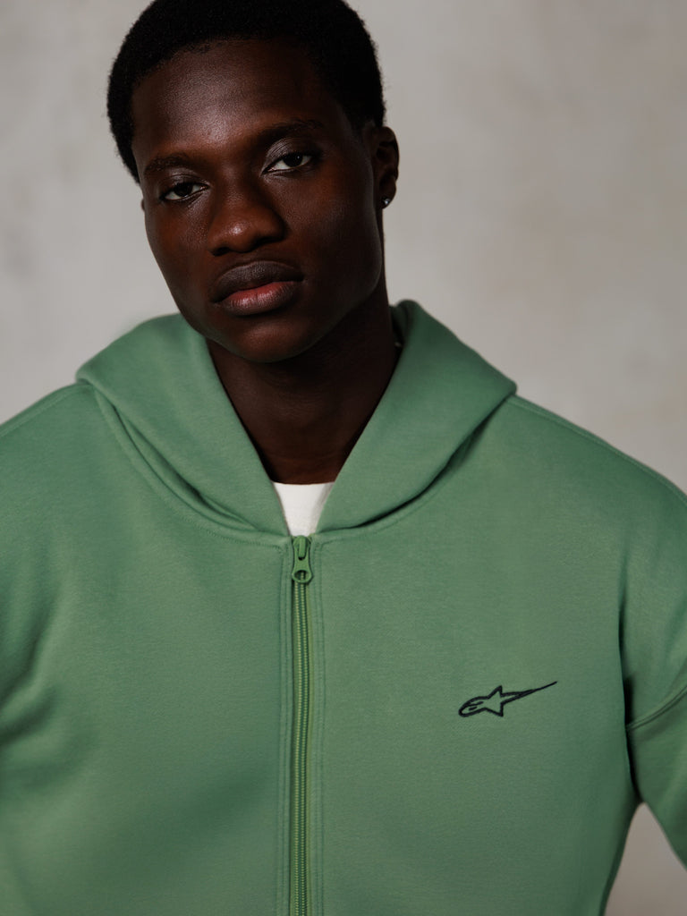 Alpinestars Essentials Ageless Zip Hoodie, Lifestyle-Porträt, kaktusgrün mit kleinem schwarzem Logo, Reißverschluss vorne, weiche Fleece-Struktur, lässige, vom Motorsport inspirierte Streetwear