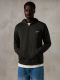 Alpinestars Essentials Ageless Zip Hoodie, Off Black, Zip-Kapuzenjacke mit einem kleinen weißen Alpinestars-Logo auf der Brust, entspannte Passform, getragen von einem Modell mit blauen Jeans und einem weißen T-Shirt, lässige vom Motorsport inspirierte Streetwear