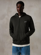 Alpinestars Essentials Ageless Zip Hoodie, Off Black, Zip-Kapuzenjacke mit einem kleinen weißen Alpinestars-Logo auf der Brust, entspannte Passform, getragen von einem Modell mit blauen Jeans und einem weißen T-Shirt, lässige vom Motorsport inspirierte Streetwear
