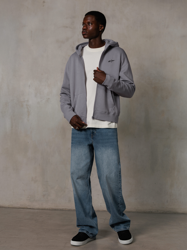 Alpinestars Essentials Ageless Zip Hoodie, Silber, lässige Streetwear, Fleece-Kapuzenjacke mit Reißverschluss, kleines schwarzes Logo auf der Brust, getragen von einem Model mit weißem T-Shirt und blauer Jeans, entspannte Lifestyle-Passform