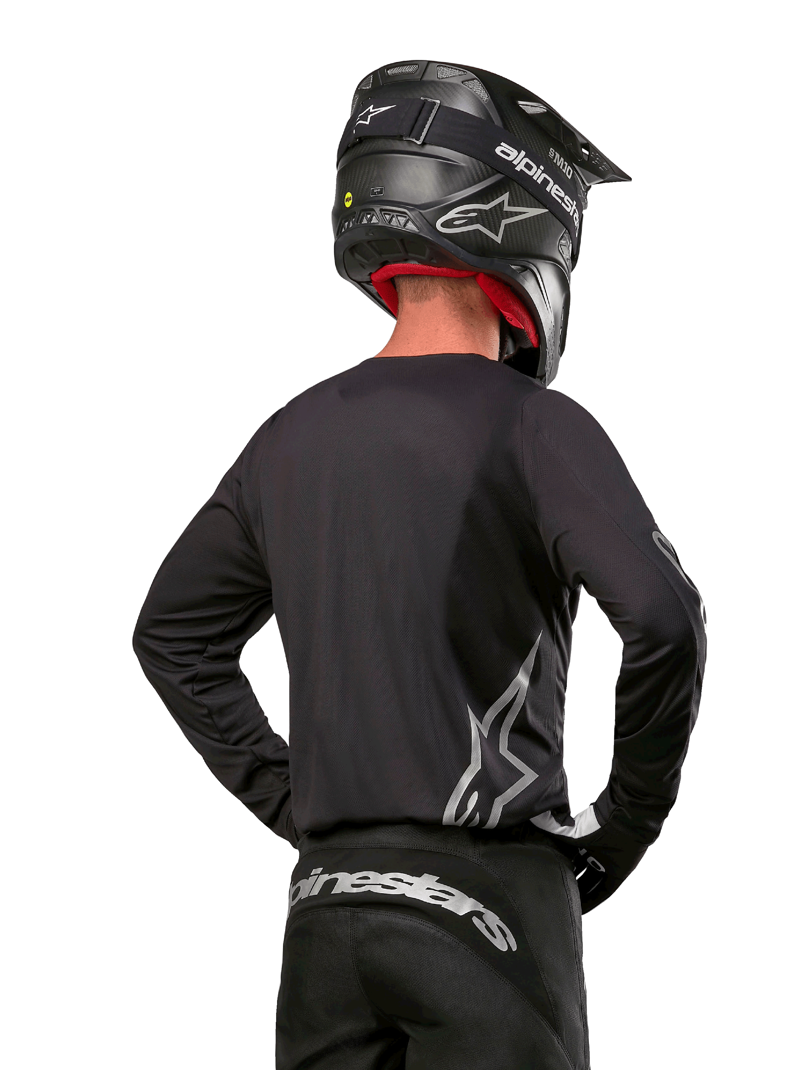 Motocross-Fahrer in der Rückansicht, trägt das Alpinestars 2024 Fluid Graphite Jersey in Black Silver mit einem großen silbernen Logo an der Seite, kombiniert mit einem schwarzen Helm in Carbon-Optik und einer schwarzen Hose, professionelle Offroad-Rennausrüstung