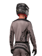 Motocross-Fahrer in der Rückansicht, trägt das Alpinestars 2024 Fluid Lurv Trikot in Mud Black, mit schwarzem Alpinestars-Branding auf Ärmeln und Rücken, kombiniert mit einem schwarzen Helm und passender Ausrüstung für den Offroad-Rennsport