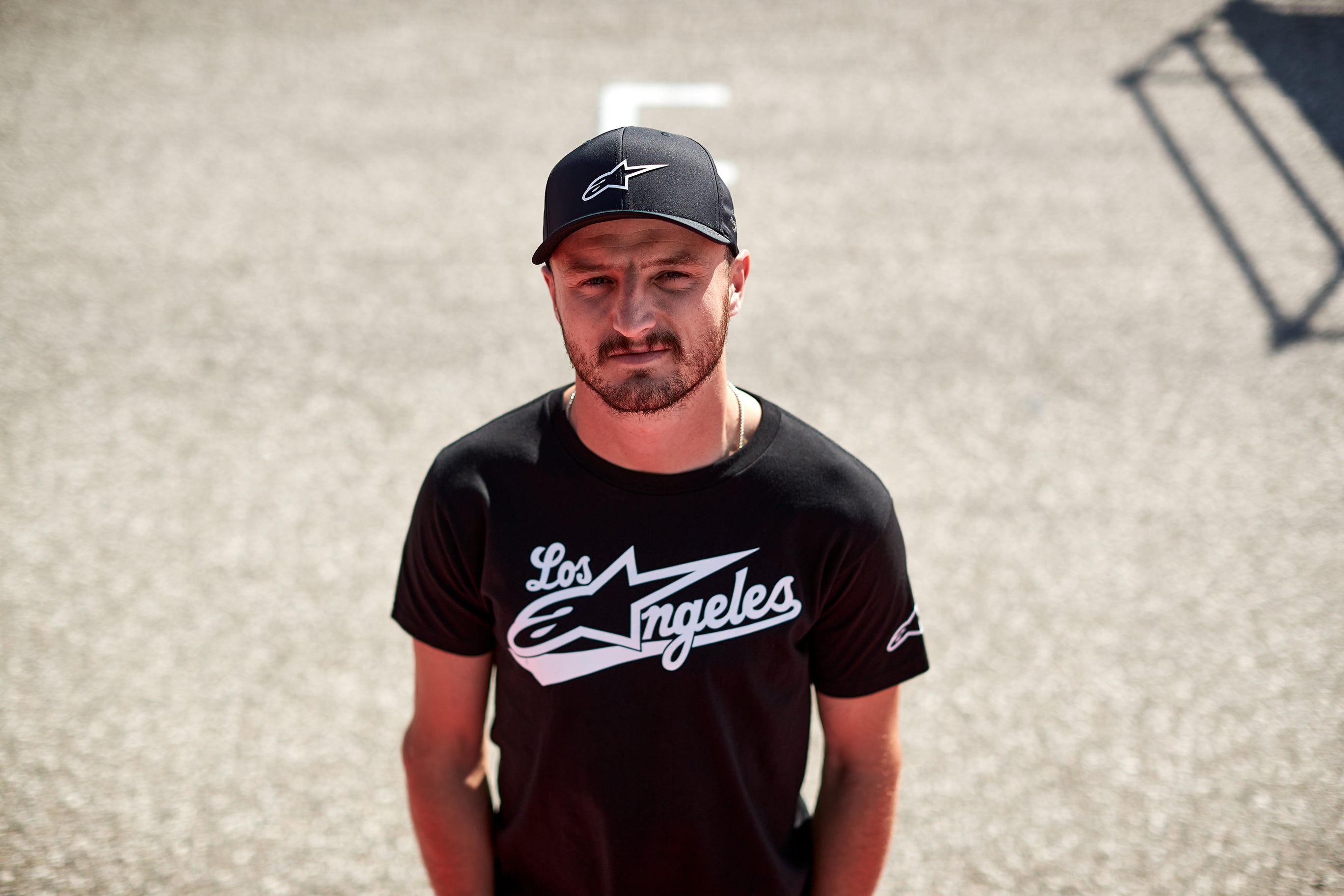 Jack Miller wearing a black t-shirt with 'Los Angeles' and a cap with Alpinestars logo on a textured wall background