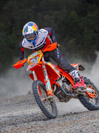 Motocross-Fahrer in Aktion im Alpinestars Pro-Dura Jersey in Schwarz, leuchtendem Rot und Weiß, fährt ein orangefarbenes Dirtbike auf einem staubigen Offroad-Trail, kombiniert mit einer schwarzen Hose und rot-weißen Stiefeln