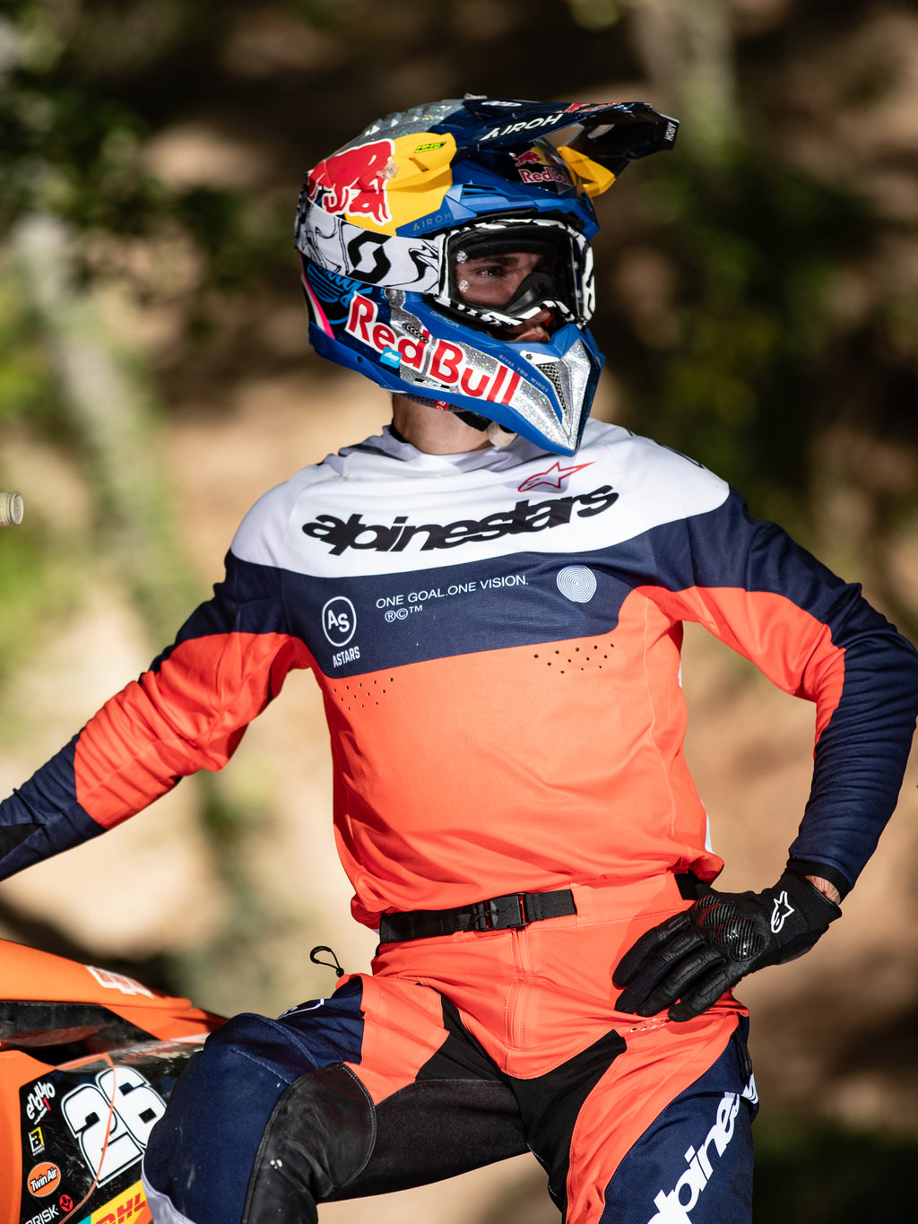 Motocross-Fahrer im Alpinestars Pro-Dura Trikot in Navy, Hot Orange und Weiß, mit markantem Branding auf der Brust und Laser-Perforationen, kombiniert mit einem Red Bull Rennhelm, professionelle Ausrüstung für Enduro- und Offroad-Performance.