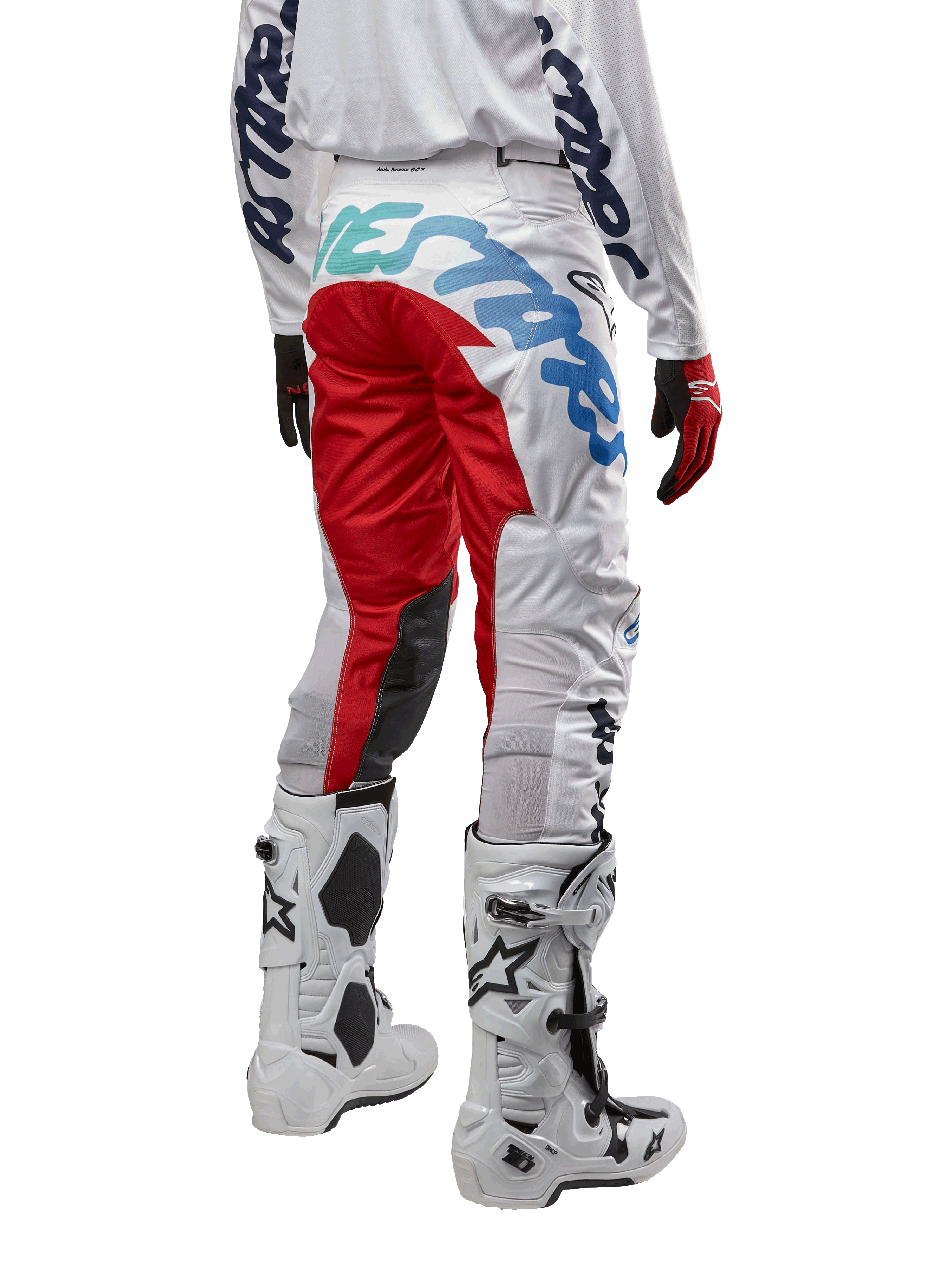 Alpinestars 2024 Racer Hana Hose, Motocross-Hose, Weiß Mehrfarbig mit roten und blauen Akzenten, Rückansicht mit großem Branding am Gesäß, getragen mit weiß-schwarzen Motocross-Stiefeln, entwickelt für Offroad-Performance und Langlebigkeit