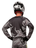 Alpinestars 2024 Racer Tactical Trikot, Motocross-Trikot, Cast Gray Camo Magnet, Rückansicht mit grauem und schwarzem Tarnmuster, getragen mit passender Hose und einem schwarz-weißen Helm, professionelle Offroad-Rennausrüstung