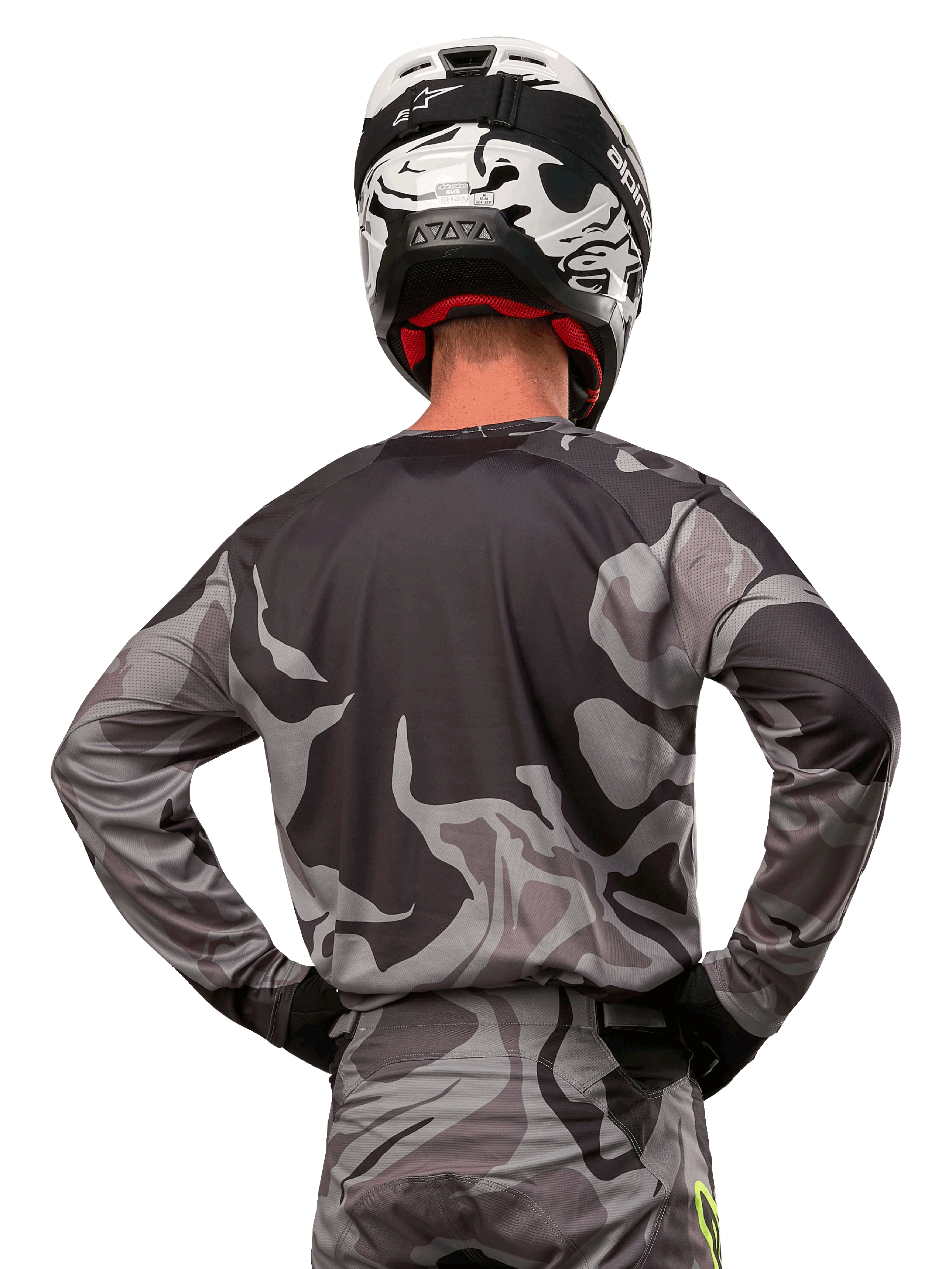 Alpinestars 2024 Racer Tactical Trikot, Motocross-Trikot, Cast Gray Camo Magnet, Rückansicht mit grauem und schwarzem Tarnmuster, getragen mit passender Hose und einem schwarz-weißen Helm, professionelle Offroad-Rennausrüstung
