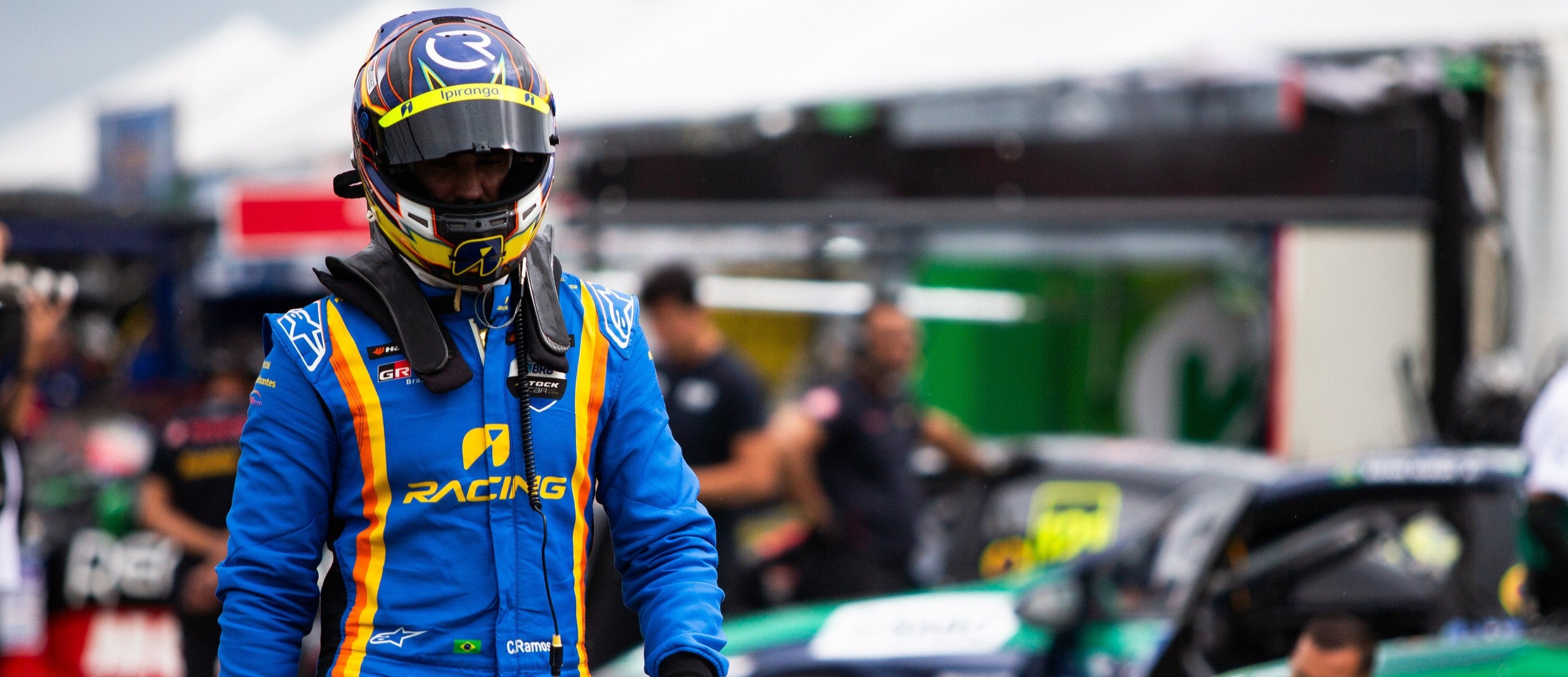 Alpinestars Tech Vision V3 Custom Suit, blue and yellow FIA racing suit worn by a driver in the pit lane.