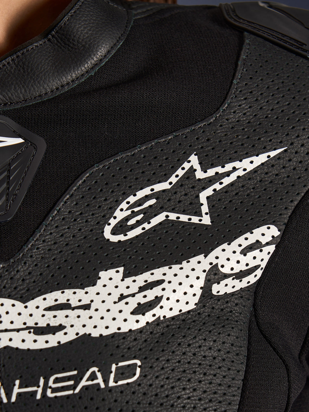 Nahaufnahme des Alpinestars Stella GP-R7 2-Teiler-Lederanzugs in Schwarz, mit perforierten Lederbahnen, einem großen weißen Alpinestars-Logo auf der Brust und atmungsaktiven Stretchgewebe-Abschnitten.
