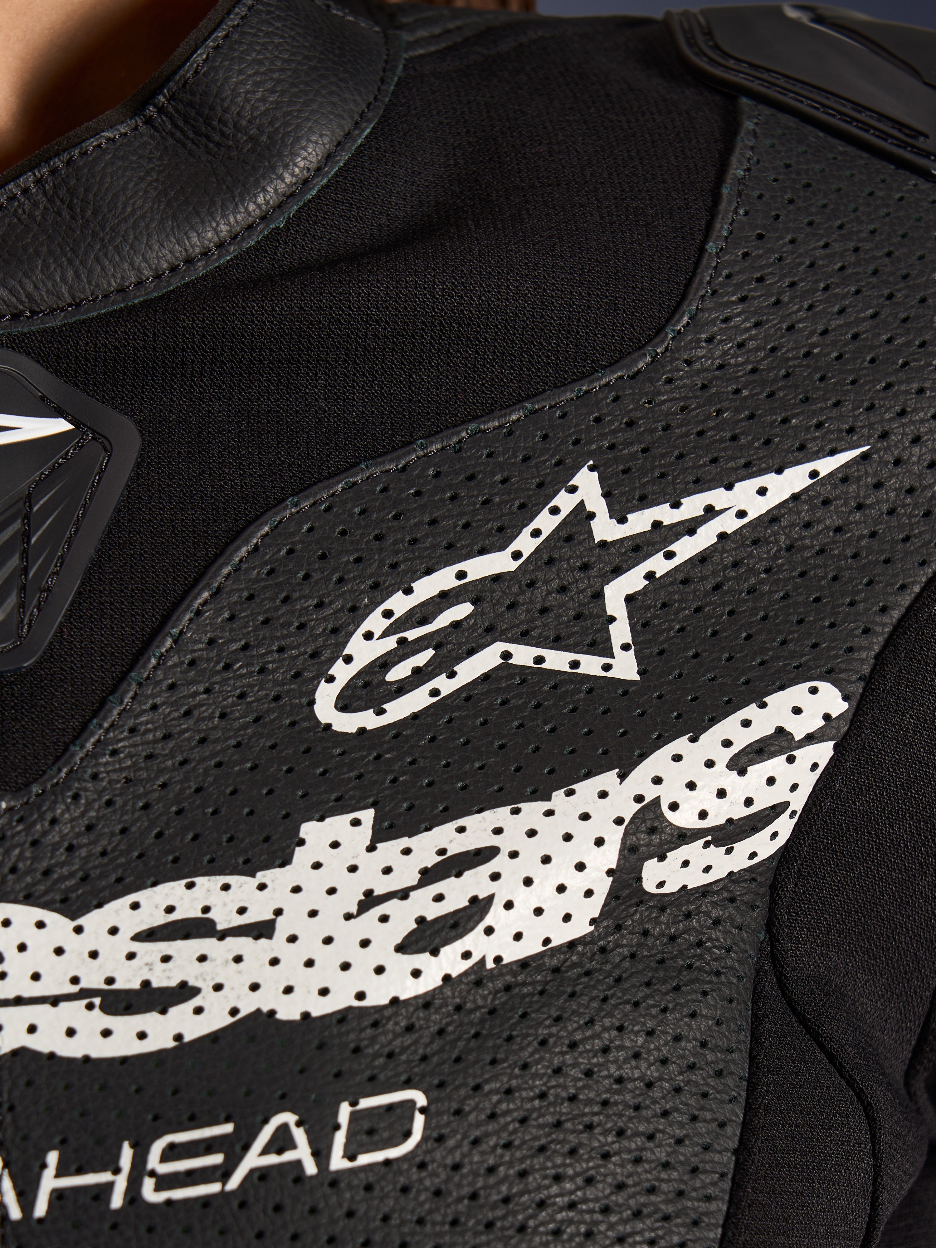 Nahaufnahme des Alpinestars Stella GP-R7 2-Teiler-Lederanzugs in Schwarz, mit perforierten Lederbahnen, einem großen weißen Alpinestars-Logo auf der Brust und atmungsaktiven Stretchgewebe-Abschnitten.