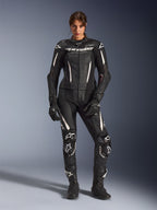 Frau im Alpinestars Stella GP-R7 2-Teiler Lederanzug in Schwarz mit weißen Akzenten, mit perforierten Lederpaneelen und weißem Branding auf Brust und Knien, kombiniert mit passenden schwarzen Rennhandschuhen und Stiefeln, professionelle Motorrad-Rennausrüstung