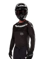 Alpinestars 2024 Supertech Ward Trikot, Motocross-Trikot, Schwarz und Weiß, langärmelige Performance-Ausrüstung mit markantem Alpinestars-Branding, getragen mit passendem Helm und Handschuhen, athletische Passform für den Offroad-Sport