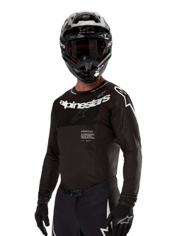Alpinestars 2024 Supertech Ward Trikot, Motocross-Trikot, Schwarz und Weiß, langärmelige Performance-Ausrüstung mit markantem Alpinestars-Branding, getragen mit passendem Helm und Handschuhen, athletische Passform für den Offroad-Sport