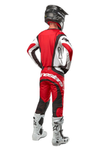 Alpinestars 2024 Techstar Ocuri Pants, Motocross Pants, Mars Red White Black, rear view of a motocross rider wearing full racing gear, including matching jersey, black helmet, and white and black boots, highlighting the Alpinestars branding and durable fabric construction.