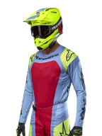 2024 Techstar Ocuri Jersey, Motocross-Rennsport-Trikot, Hellblau mit roten und neongelben Akzenten, getragen mit passendem neongelbem Helm und schwarzer Brille, mit schwarzen Alpinestars-Logos auf Brust und Schultern, sportliches, rennsportinspiriertes Design für Offroad-Performance