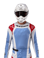Alpinestars 2024 Techstar Ocuri Trikot, Motocross-Renntrikot, Hellblau, Mars-Rot und Weiß, Vorderansicht mit lasergeschnittener Belüftung und athletischer Passform, getragen mit weißem Helm und Brille für einen professionellen Offroad-Rennlook