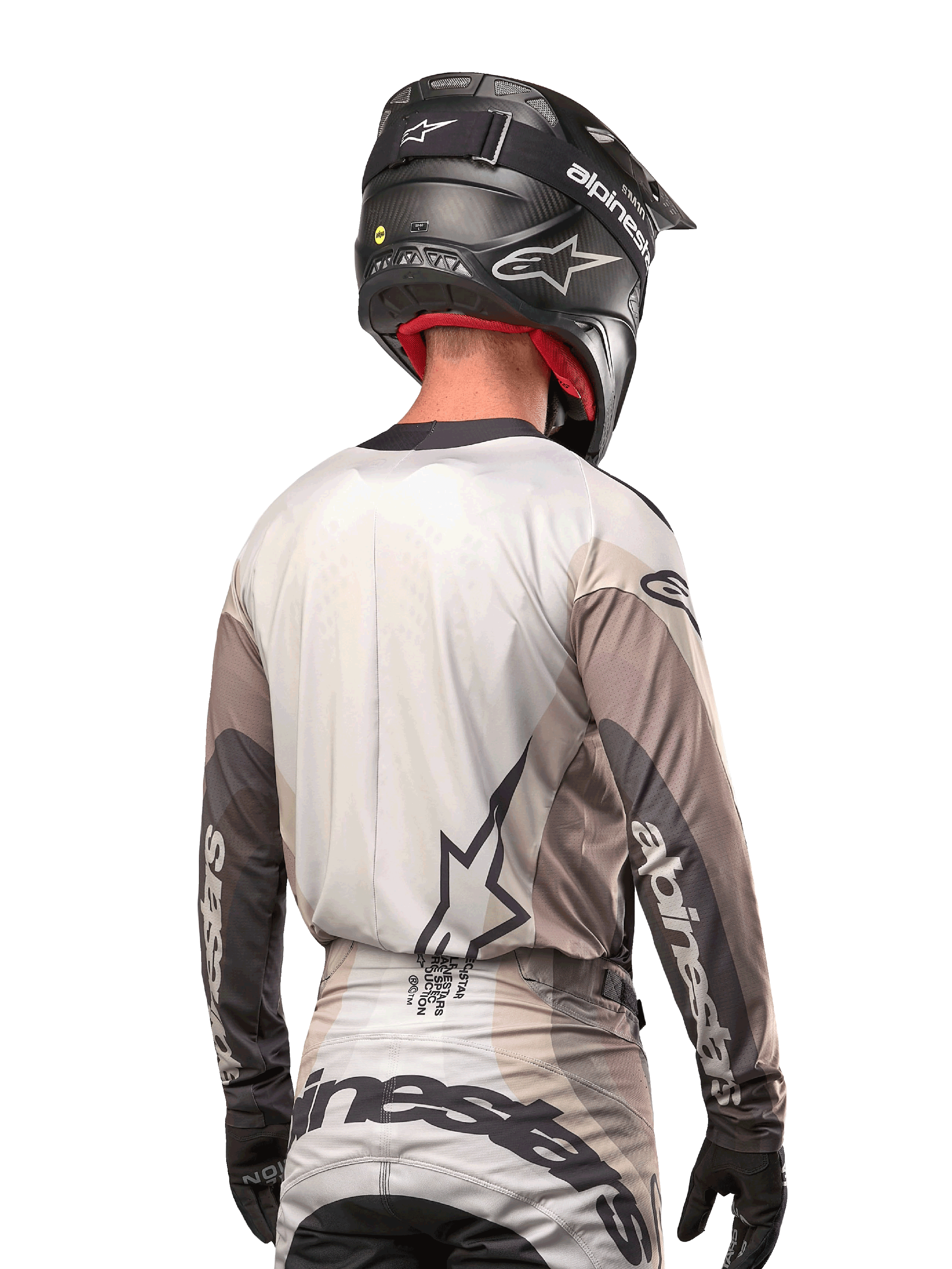 Motocross-Fahrer von hinten im Alpinestars 2024 Techstar Pneuma Jersey in Dark Sand Iron Dust Gray, kombiniert mit einem schwarzen Helm mit Carbon-Finish, mit einem großen Stern-Logo auf dem Rücken und Alpinestars-Branding auf den Ärmeln.