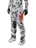 Alpinestars 2024 Techstar Rantera Hose, Motocross-Hose, Haze Gray Camo mit schwarzem und rotem abstraktem Muster, getragen mit passendem Jersey, schwarzen Handschuhen und weißen Motocross-Stiefeln, konzipiert für Hochleistungs-Offroad-Rennsport