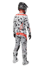 Motocross-Fahrer von hinten in Alpinestars 2024 Techstar Rantera Hose, Haze Gray Camo mit schwarzen Flecken und roten Logos, passendes Trikot, schwarzer Helm und weiße Stiefel, komplettes Offroad-Rennoutfit