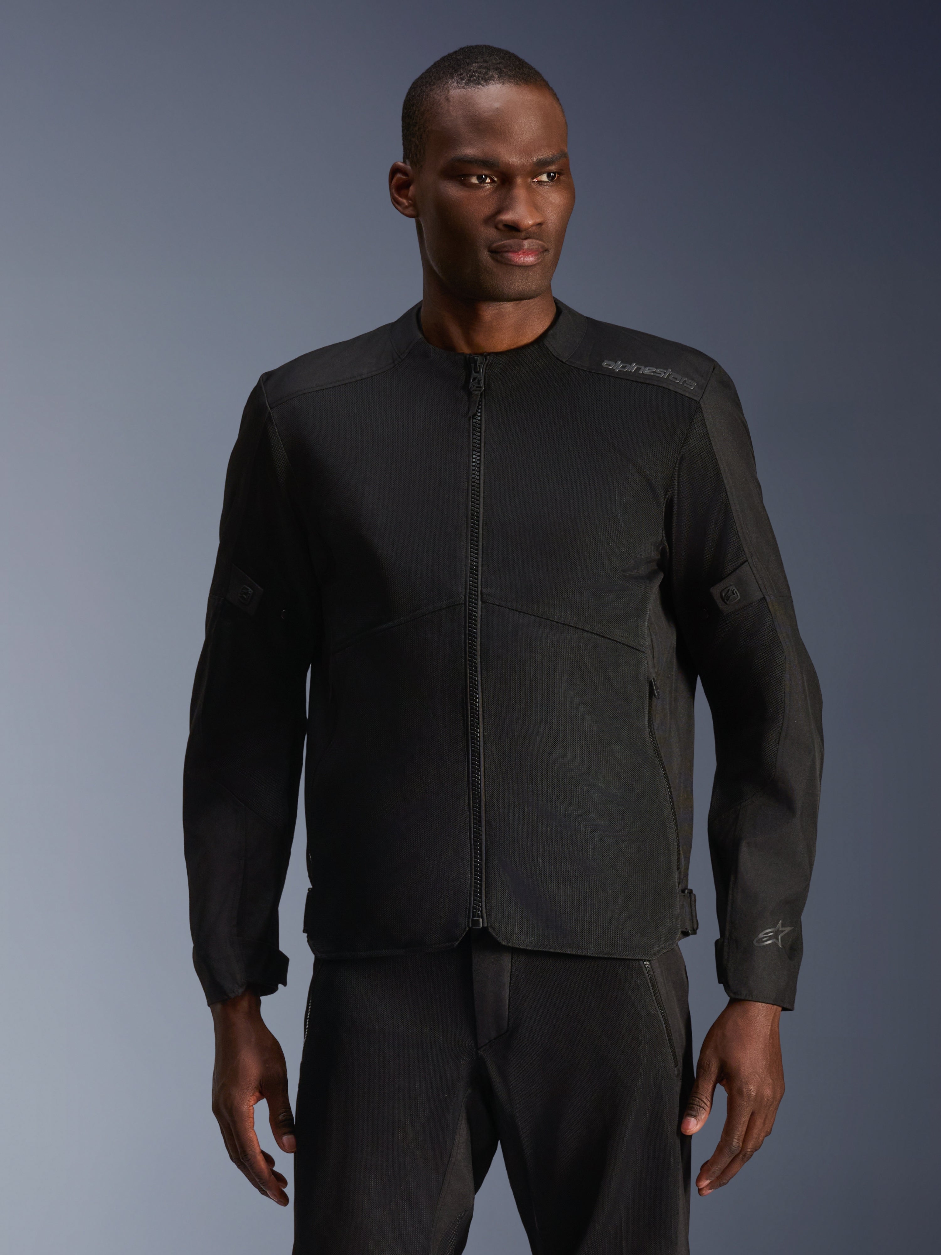 Männliches Model trägt die Alpinestars C-1 Air Jacke in Schwarz, moderne Motorradjacke mit großflächigen Tech-Mesh-Einsätzen und durchgehendem Frontreißverschluss, kombiniert mit passender schwarzer Motorradhose, urbane Lifestyle- und Pendler-Ästhetik