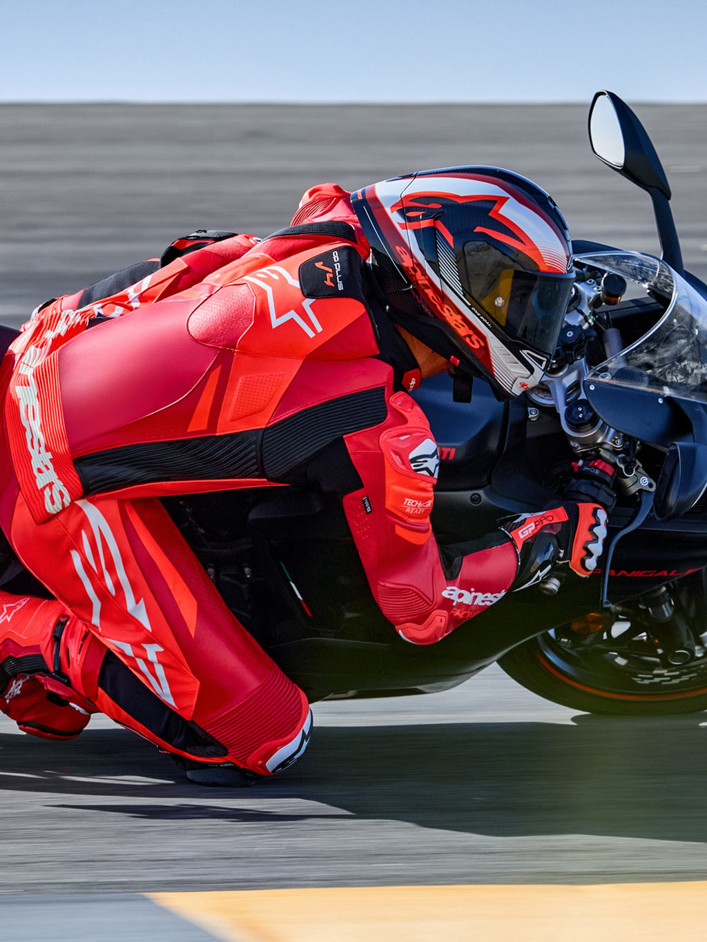 Alpinestars GP Plus V4 Sprint Lederkombi, Tech-Air® Ready, Fluo-Rot und Weiß, Motorradfahrer in Schräglage auf Rennstrecke.