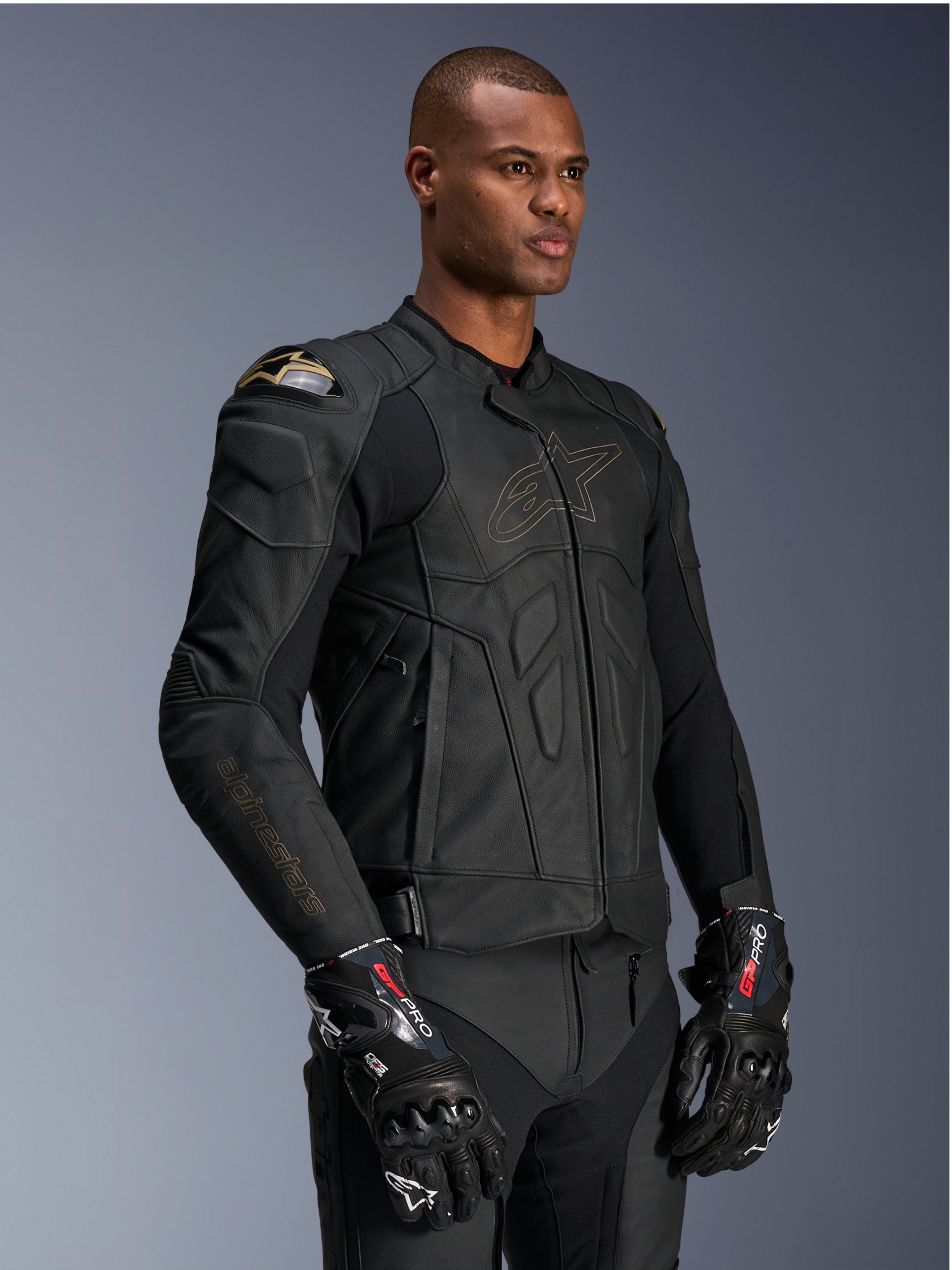 Alpinestars Dusk Leather Jacket, Black Laser motorcycle jacket, premium leather construction with gold Alpinestars logo outline and sleeve branding, external DFS shoulder protection, paired with GP Pro gloves, performance racing gear