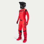 Motocross-Fahrer in kompletter Rennausrüstung, Supertech Ember LE Trikot und Hose in Rot Fluo und Schwarz, schwarzer Helm mit Goggles, passende rote und schwarze Stiefel und Handschuhe, abgestimmtes Profi-Outfit für den Offroad-Rennsport