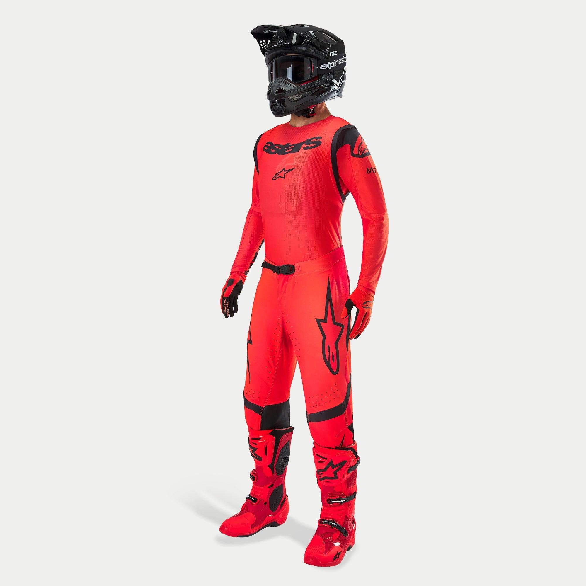 Motocross-Fahrer in kompletter Rennausrüstung, Supertech Ember LE Trikot und Hose in Rot Fluo und Schwarz, schwarzer Helm mit Goggles, passende rote und schwarze Stiefel und Handschuhe, abgestimmtes Profi-Outfit für den Offroad-Rennsport