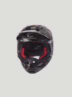 Alpinestars Supertech M10 Solid Helmet ECE 22.06, Black Glossy Carbon Motocross Helmet with red interior padding. High-performance off-road racing protection featuring a 3K carbon shell, MIPS technology, and 28-port ventilation system for maximum airflow.